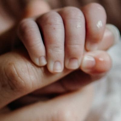 Main d'un nouveau né accroché au doigt de sa maman pendant le massage bébé