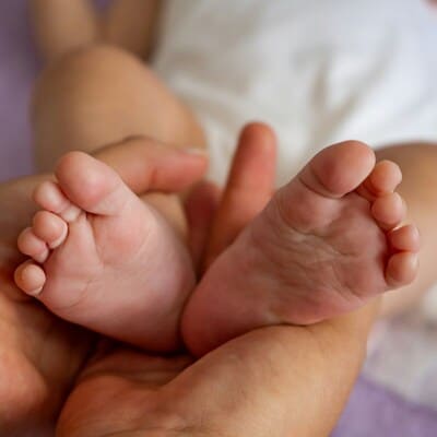 petits pieds de bébé entre les mains pour une séance de réflexologie bébé émotionnelle